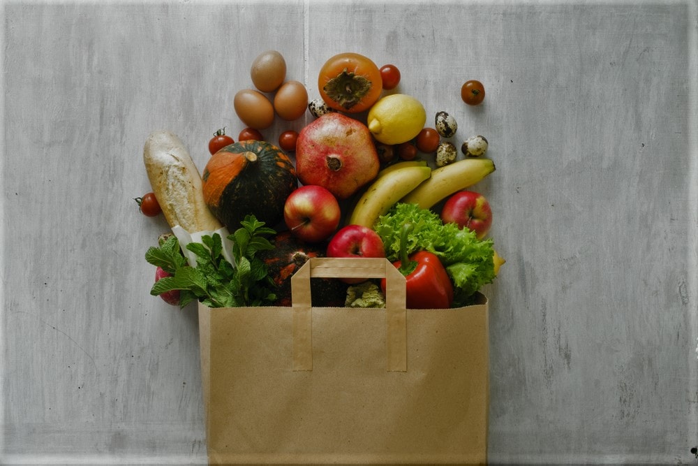 Paper bag of different health food on white wooden background. Top view. Flat lay