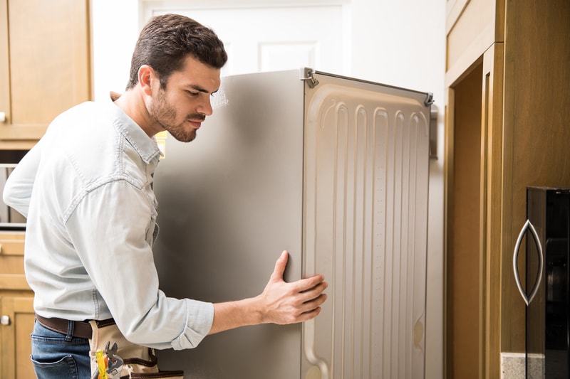 Serviceman moving fridge into position in new home